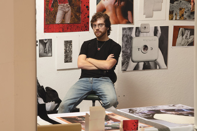 artist sitting in studio in front of images on wall